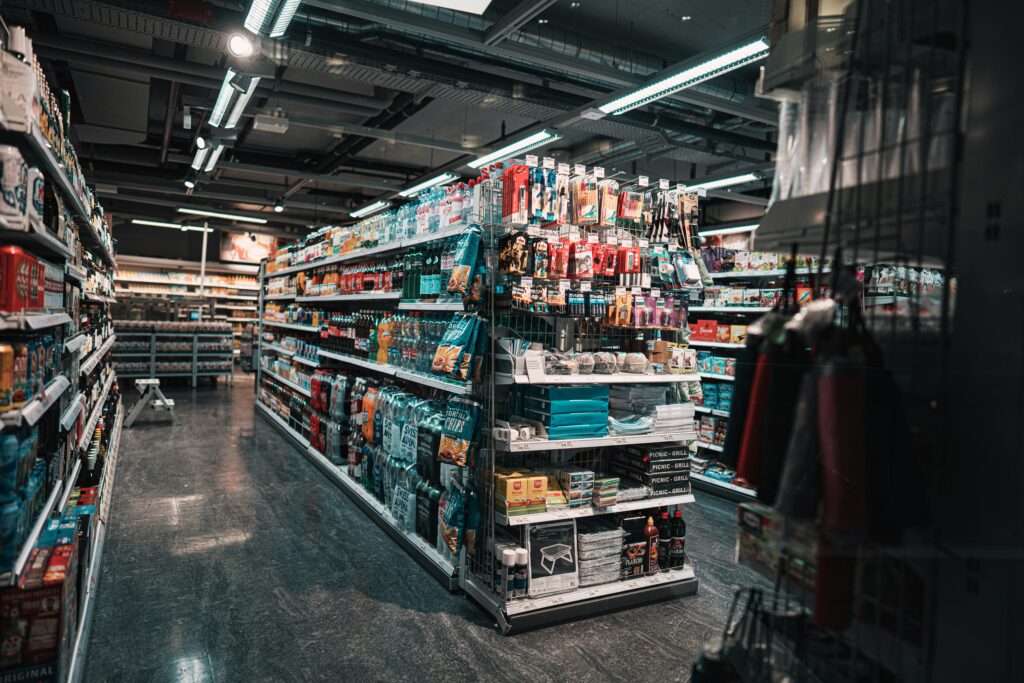 Store aisle stocked end to end, with shelves of drinks and snacks and a merchandised end-cap display.